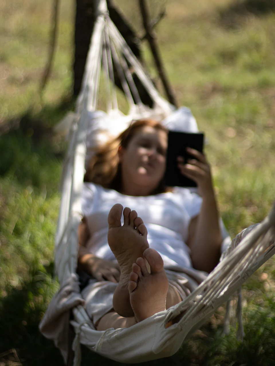 A woman stretched out in a garden hammock, smiling at her phone