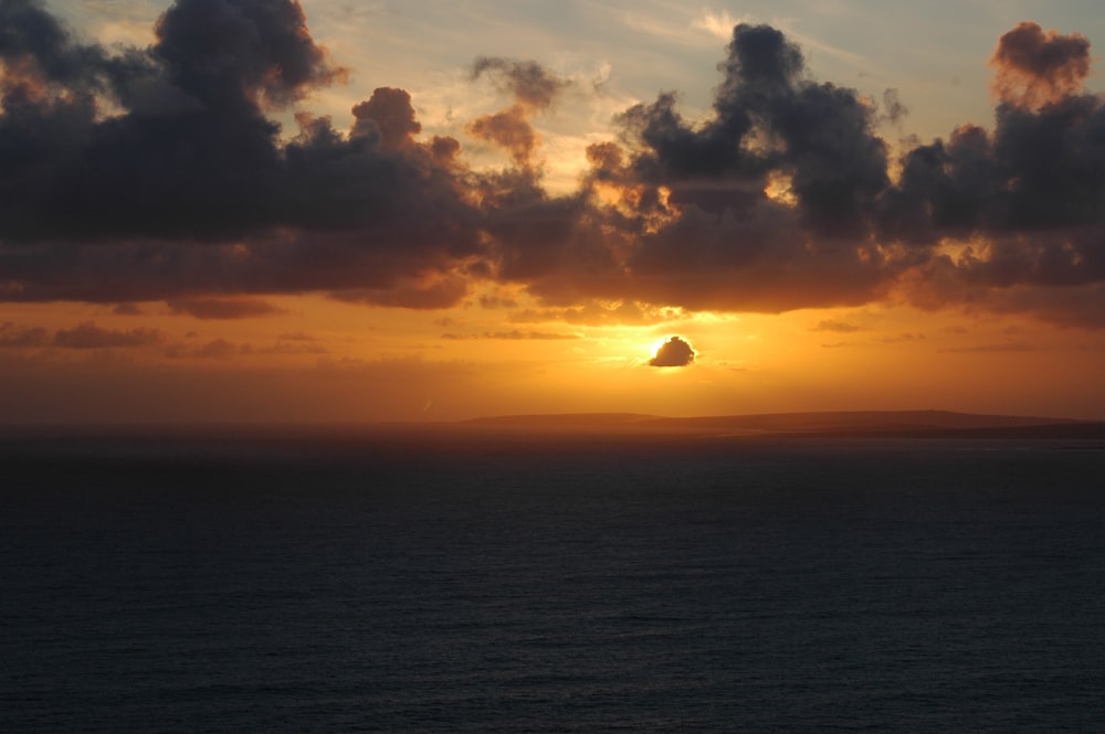 the sun setting over the ocean with clouds in the sky