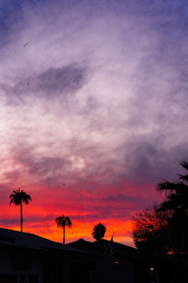 A vibrant sunset over Trancoso's iconic Quadrado, with colorful colonial houses and palm trees silhouetted against the sky.