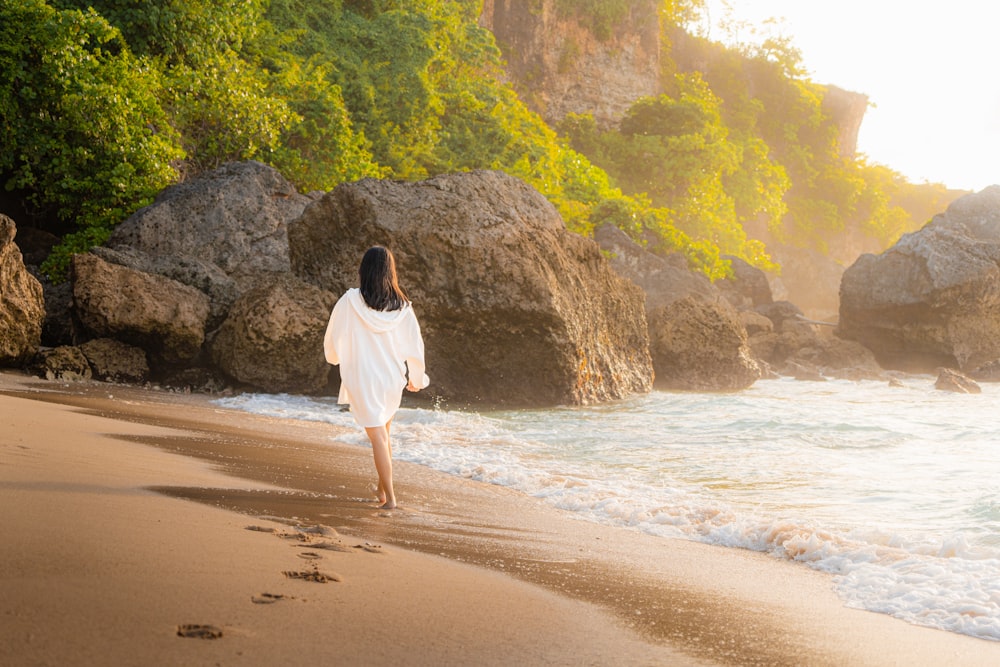 a woman walking on a beach next to the ocean