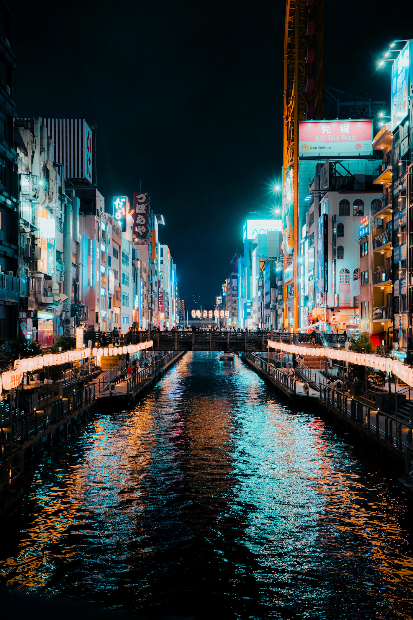 Travel photograph: Night-time signs in red, blue and yellow reflect along the Dotonbori canal.