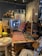 A cozy interior filled with various vintage furniture and decor items, including a woven tapestry, wooden tables and chairs, and decorative items like wooden horse sculptures and retro signs. The space has an eclectic and rustic charm, with colorful patterns and textures throughout.