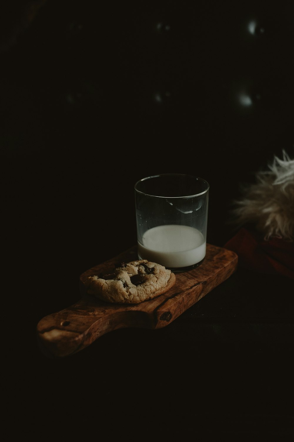 a glass of milk and a cookie on a wooden board