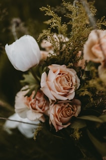A delicate bridal bouquet of soft blush roses and wild greenery resting on a rustic wooden table.