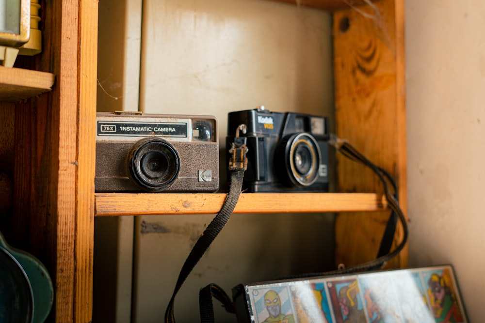 a couple of cameras sitting on top of a wooden shelf