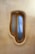 A uniquely shaped wooden-framed window with blue-tinted glass set in a textured wall. The window has an organic, asymmetrical form, reminiscent of natural shapes.