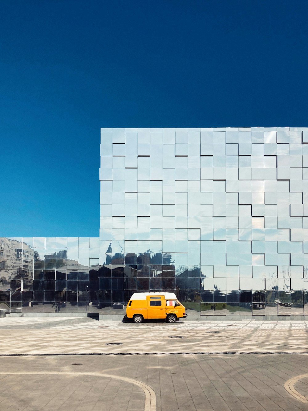 a yellow van is parked in front of a mirrored building