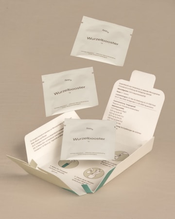 The image features a neutral-toned background with several sachets labeled 'Wurzelbooster' floating above and inside an open package. The package includes printed instructions and illustrations, suggesting a product meant for enhancing root growth. The sachets and packaging have a clean, minimalist design.