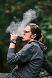 A relaxed person enjoying a vape outdoors with a soft natural background.