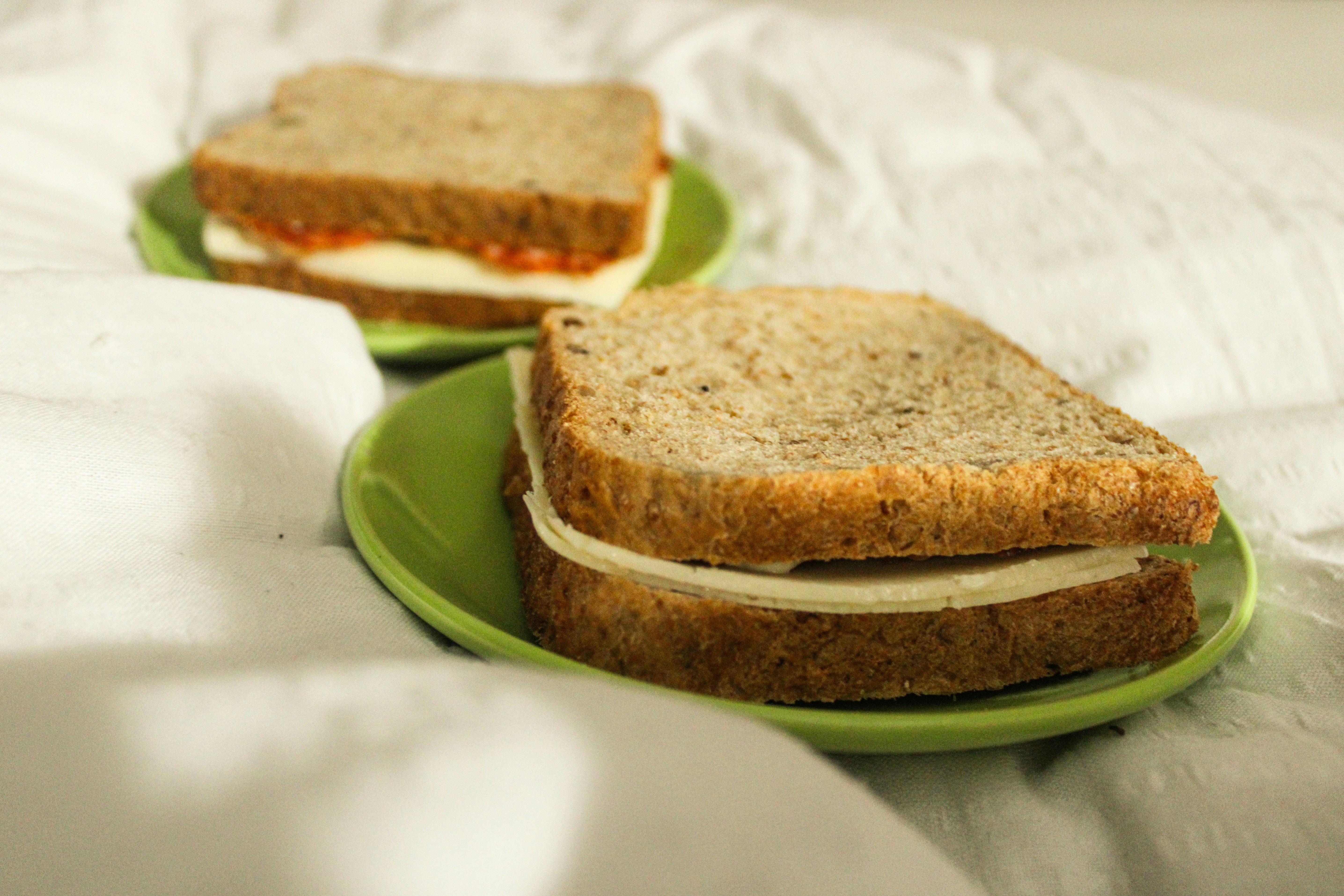 two green plates with sandwiches on them on a bed