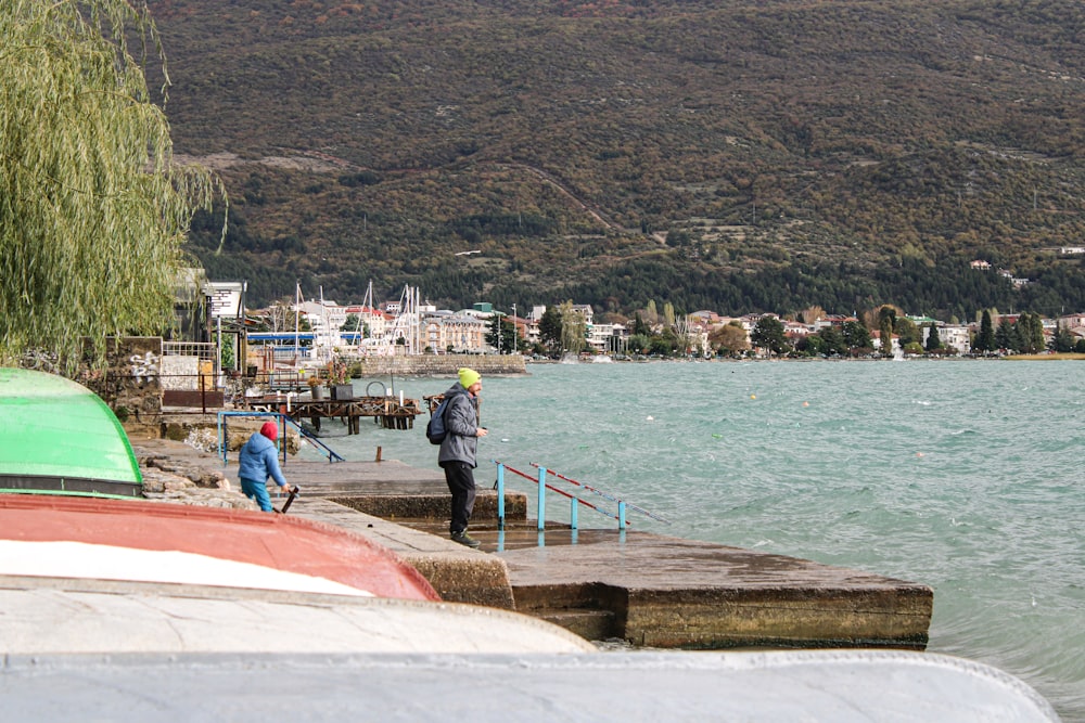 a couple of people standing on a pier next to a body of water