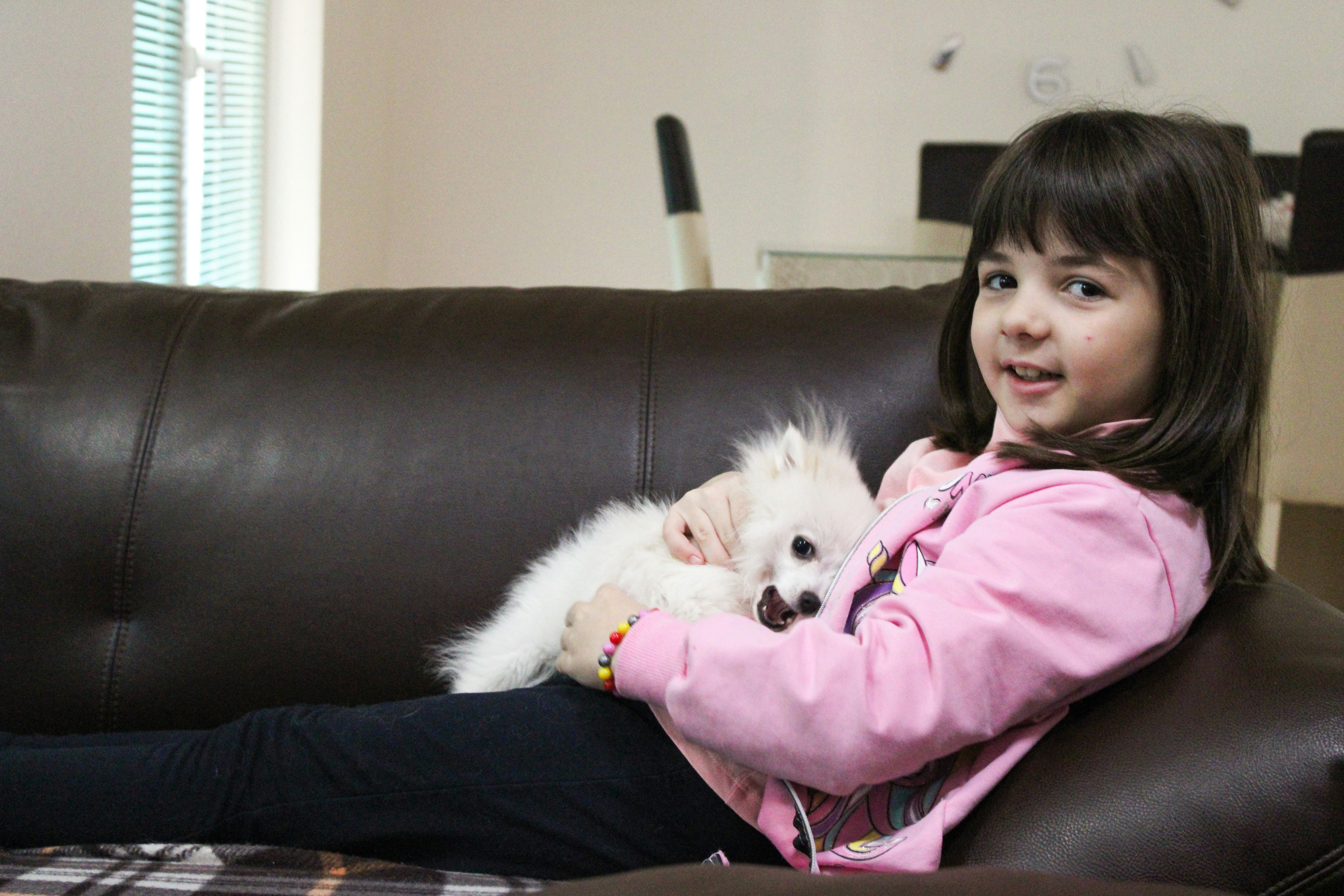 a little girl sitting on a couch holding a white dog