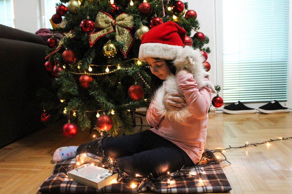 a little girl sitting on the floor next to a christmas tree