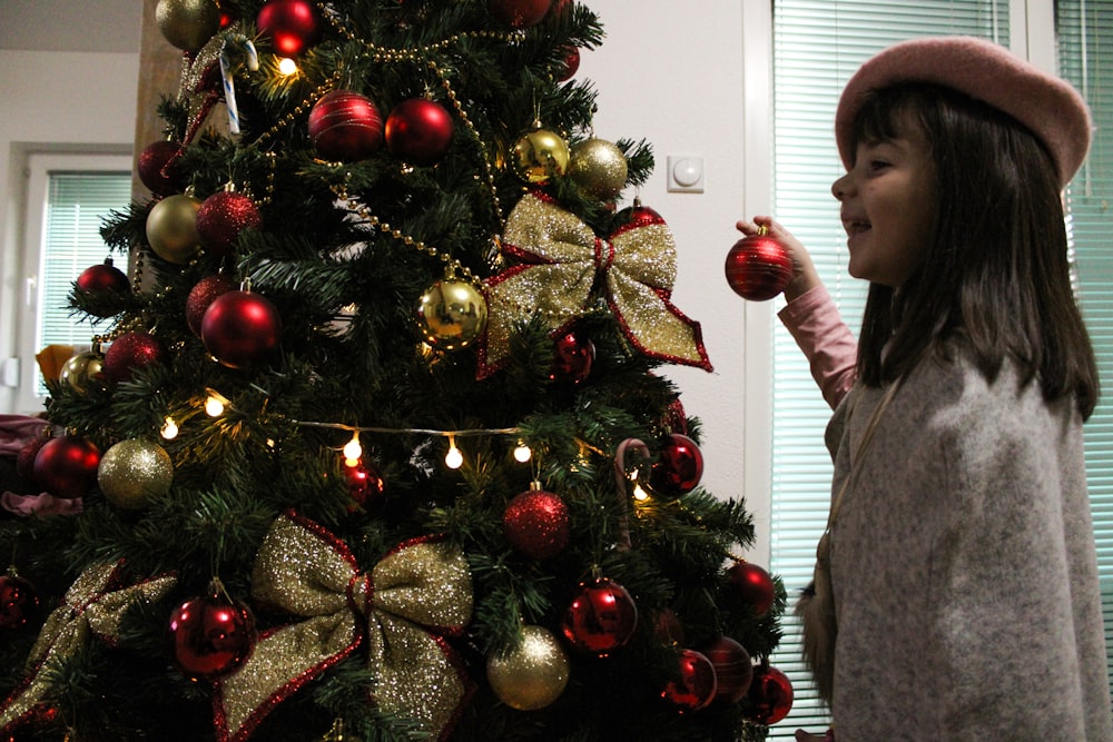 a little girl standing next to a christmas tree