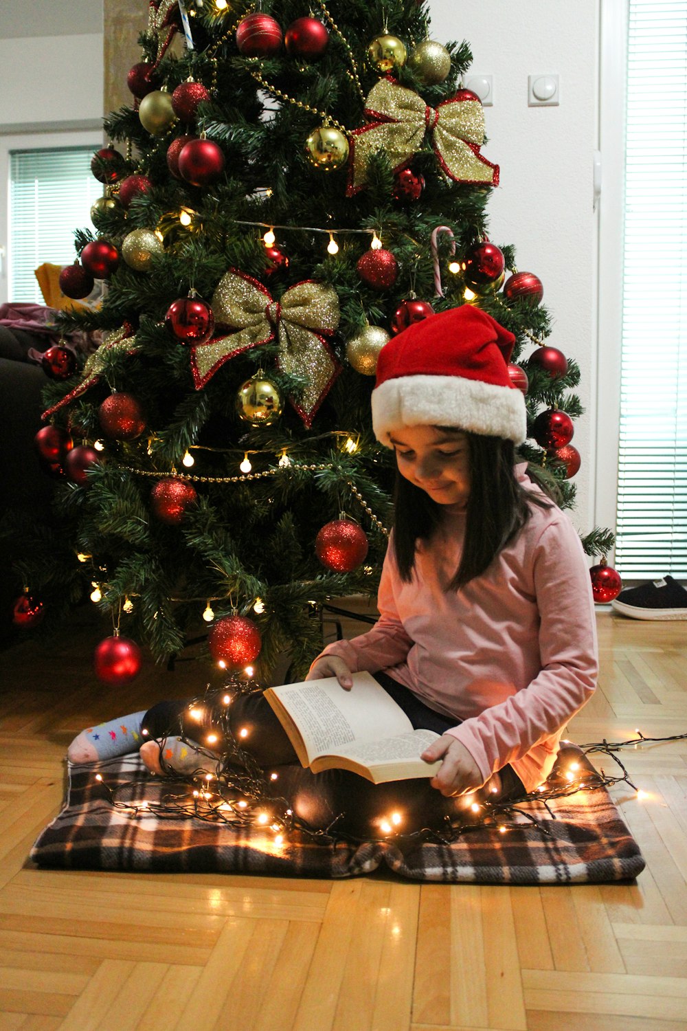 a young girl is reading a book in front of a christmas tree