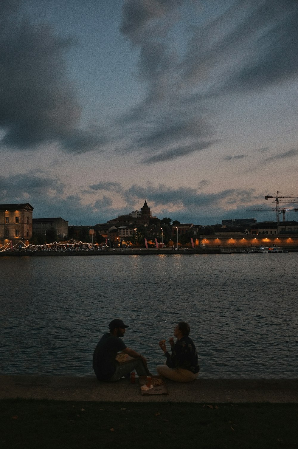 two people sitting on the edge of a body of water