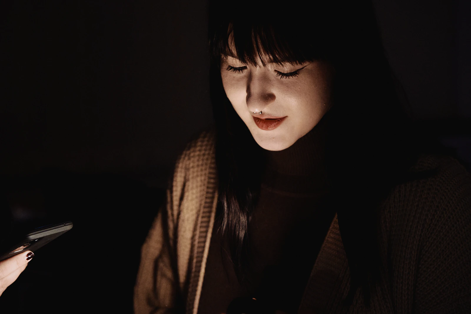 A woman looking at her phone in a dark room, her face lit by the screen, searching for answers about her symptoms late at night