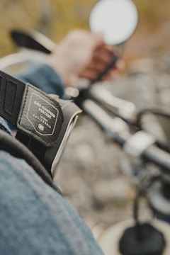 Close-up of a rally participant’s hands gripping the handlebars, with a charity logo patch on their jacket.