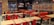 A fast-food restaurant interior with empty tables and chairs. The seating consists of a mix of red and black metal chairs and benches, with light wood tabletops. The wall features a large logo and a slogan in bold lettering. Several pendant lights hang from the ceiling, reflecting the establishment's modern design. The restaurant is well-lit, giving it a clean and inviting atmosphere.