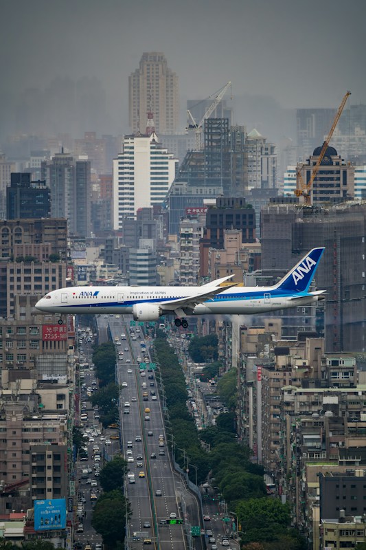 A passenger jet flying low over Taipei buildings and traffic before landing