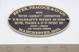 An oval metallic plaque displaying text, including the name Beyer, Peacock & Co. Ltd and details about a Beyer-Garratt locomotive. It mentions patents associated with H.W. Garratt and has patent numbers 17165, 290137, and 298422. The plaque is dated Manchester, 1930.