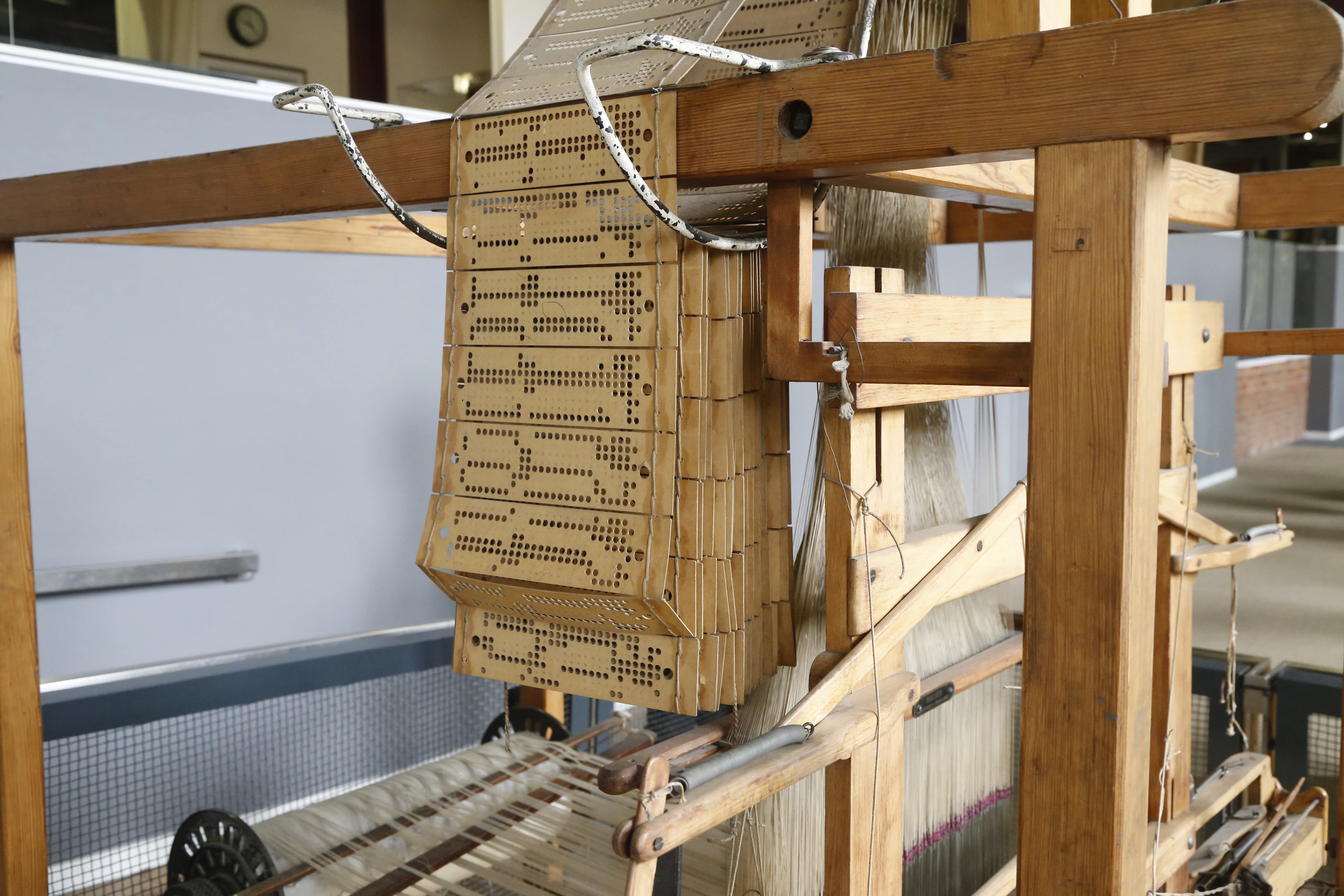 A wooden Jacquard loom in Manchester's Science and Industry Museum, its chain of punched cards hanging above taut warp threads.