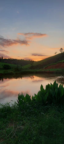 A serene landscape showing a quiet lake at sunset with soft pink and orange hues.