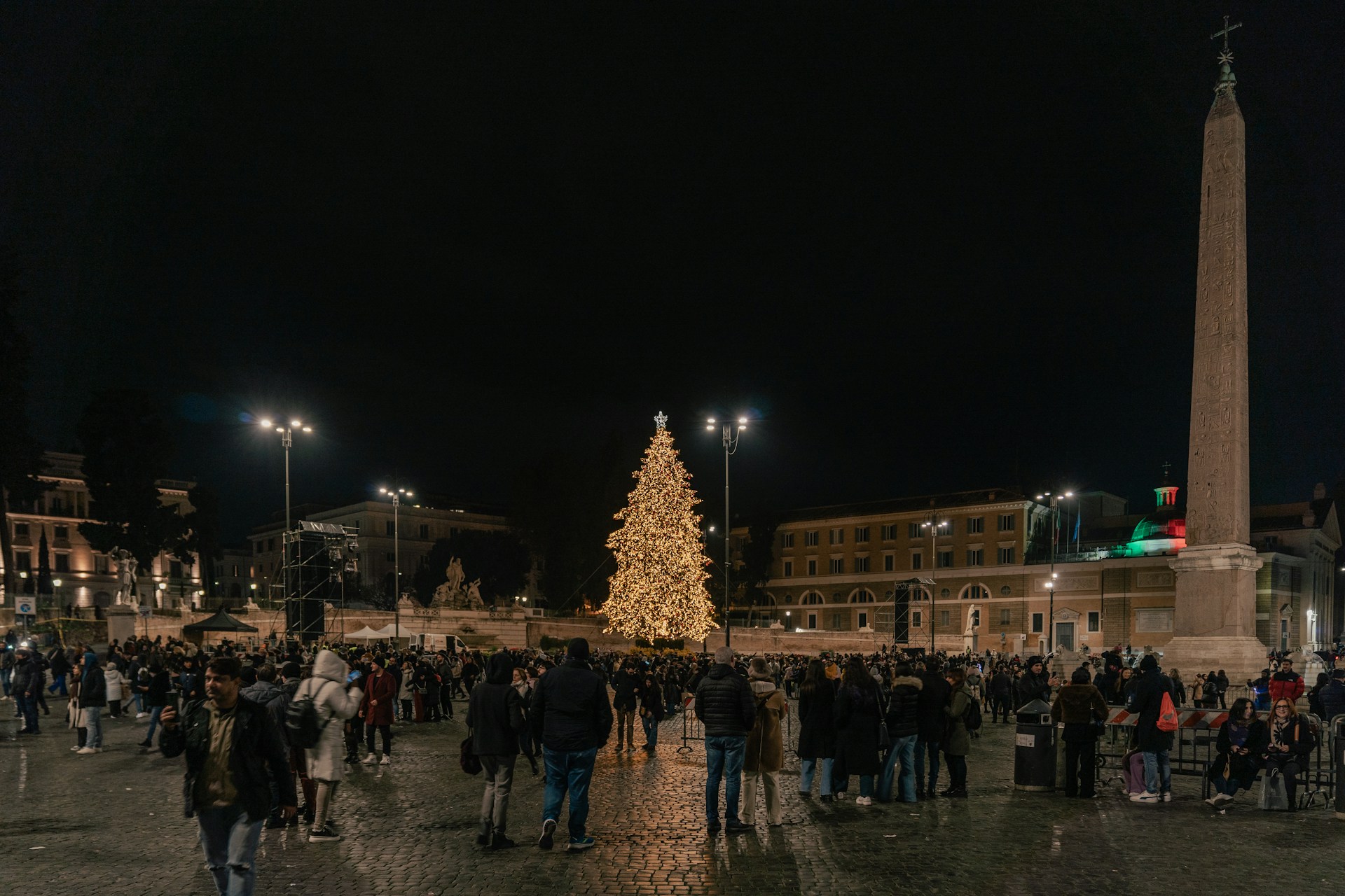 Children gathered around a large Christmas tree in the town square, smiling and enjoying holiday activities.