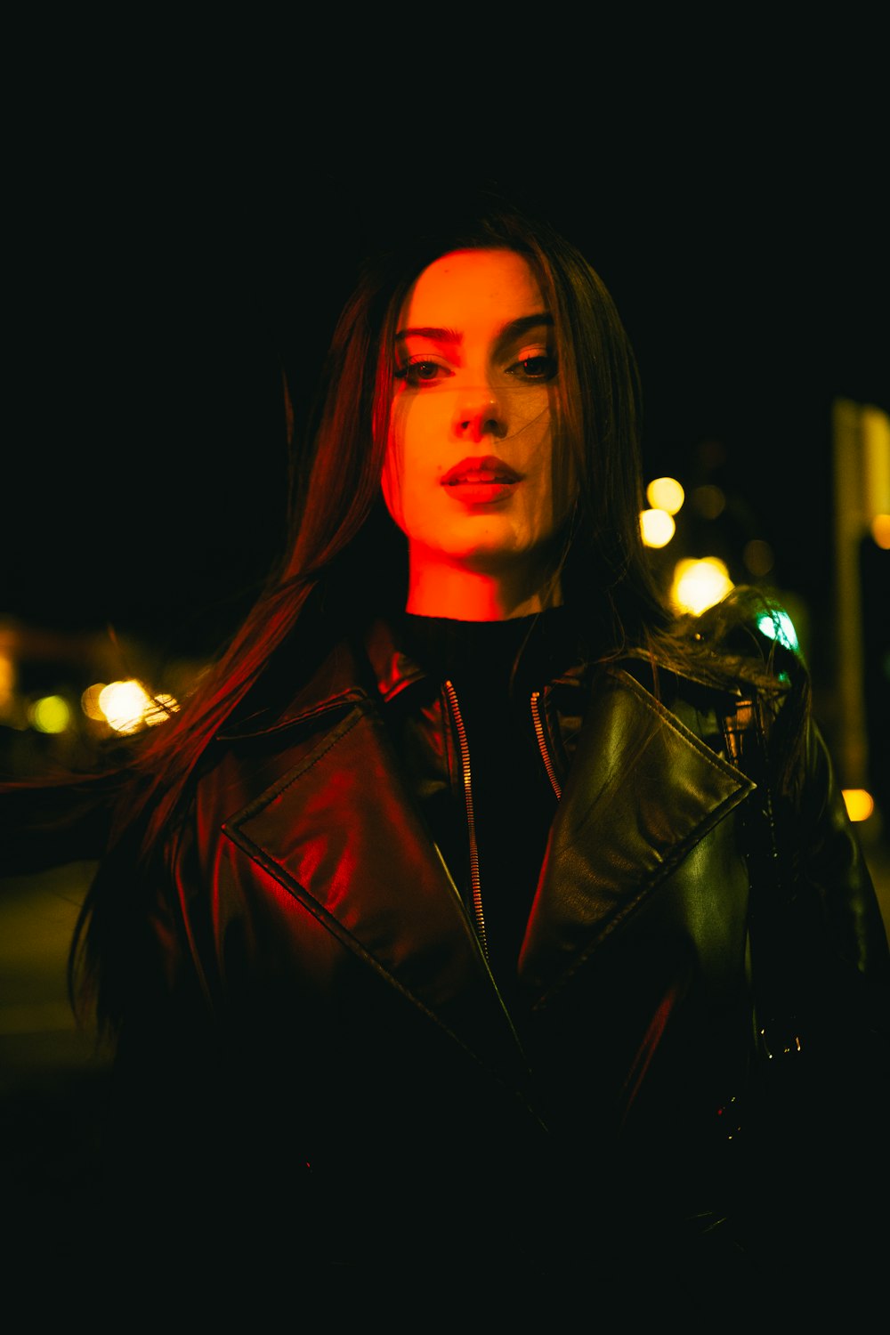 a woman in a leather jacket standing on a street at night