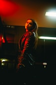 A model wearing a sleek black jacket standing against a dark urban backdrop.