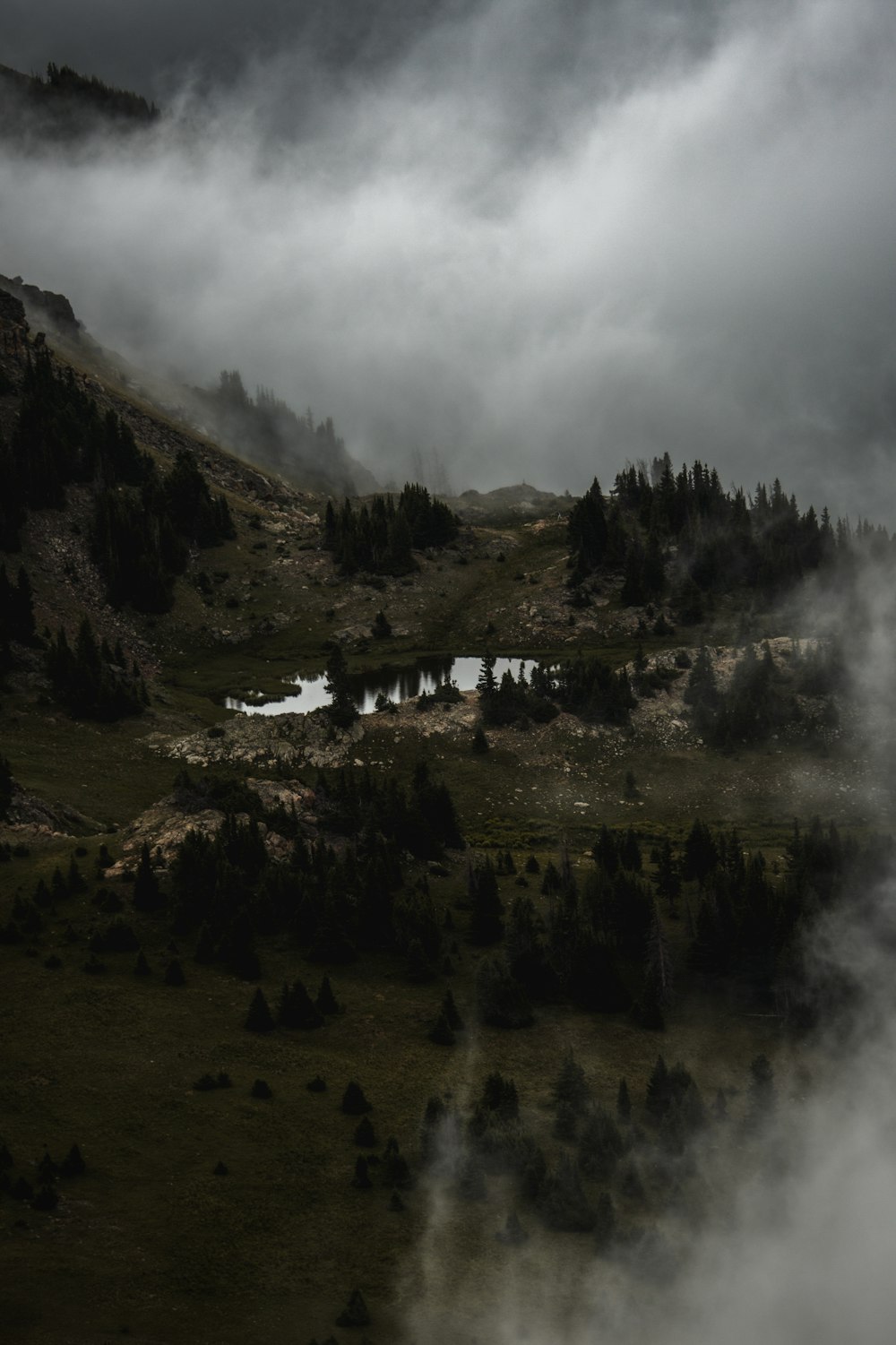 a foggy mountain with a small pond in the foreground