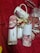 A set of items displayed on a red textured background including a decorative mug with floral and face designs, a bottle of scented home reed diffuser labeled 'Peony', and packaging with pink rose images. In the background, there are small wrapped gifts and what appears to be decorative red and white clips.