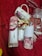 A set of items displayed on a red textured background including a decorative mug with floral and face designs, a bottle of scented home reed diffuser labeled 'Peony', and packaging with pink rose images. In the background, there are small wrapped gifts and what appears to be decorative red and white clips.