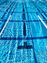 Students practicing swimming techniques in lanes with clear water and sunlight streaming in.