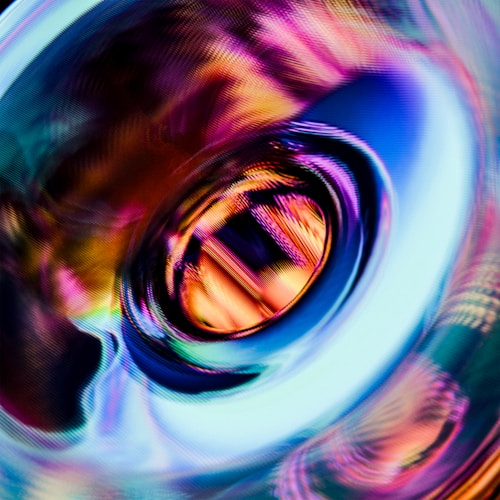 A vibrant, abstract swirl of colors creating a dynamic and fluid composition. The image features a central circular pattern with gradients of pink, purple, blue, and orange, reminiscent of a digital or liquid vortex.