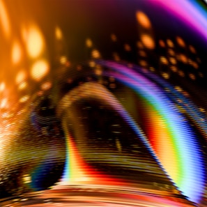 A vibrant and abstract design featuring a blend of swirling colors. The image includes streaks of bright neon hues such as purple, orange, red, yellow, and blue, creating a dynamic and energetic effect. A series of linear patterns intersect, adding texture and depth.