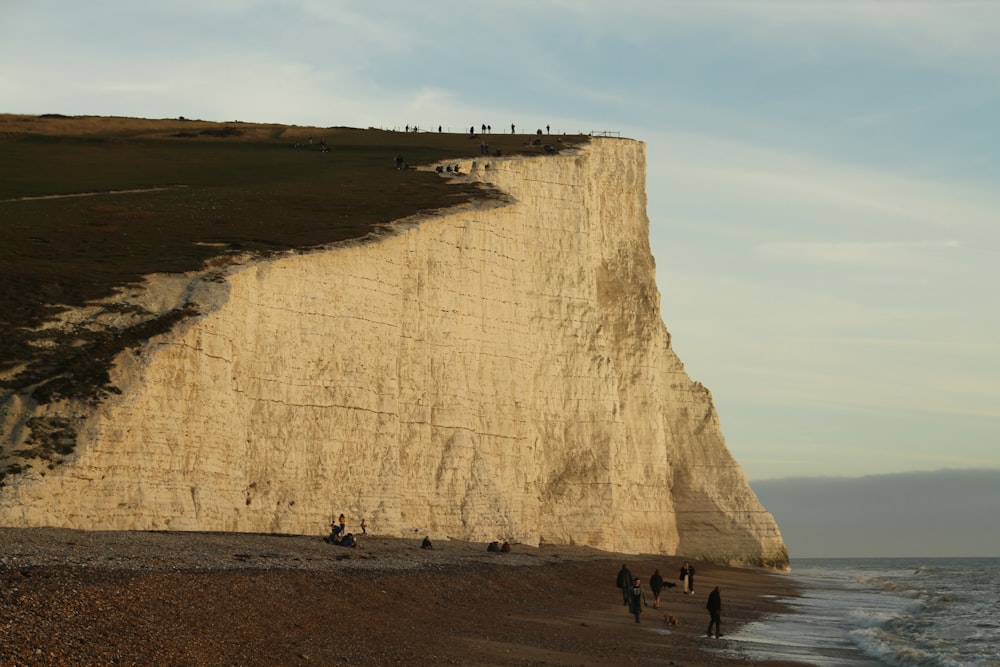 a group of people walking along a beach next to a cliff