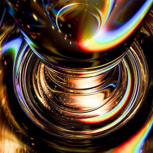 A vibrant, abstract image featuring a close-up view of a cylindrical glass object. The light refracts through the glass, creating swirling patterns of vivid colors including yellows, blues, greens, and reds. The combination of light and glass reflections gives the image a dynamic and somewhat hypnotic appearance.