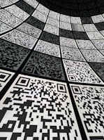 A geometric arrangement of numerous QR codes fills the perspective with a grid-like pattern. The codes are aligned in a curved fashion, creating a sense of depth and a digital, futuristic atmosphere.