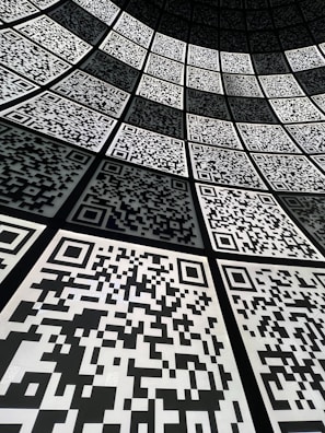 A geometric arrangement of numerous QR codes fills the perspective with a grid-like pattern. The codes are aligned in a curved fashion, creating a sense of depth and a digital, futuristic atmosphere.