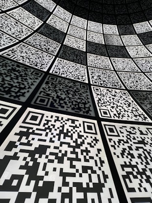 A geometric arrangement of numerous QR codes fills the perspective with a grid-like pattern. The codes are aligned in a curved fashion, creating a sense of depth and a digital, futuristic atmosphere.