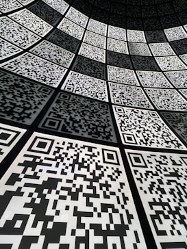 A geometric arrangement of numerous QR codes fills the perspective with a grid-like pattern. The codes are aligned in a curved fashion, creating a sense of depth and a digital, futuristic atmosphere.