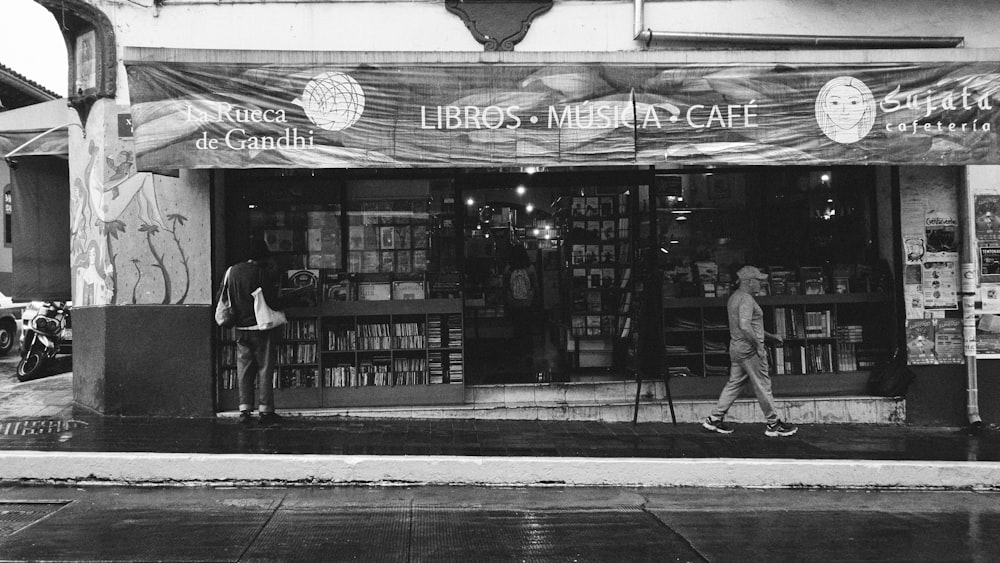 a black and white photo of people walking in front of a bookstore
