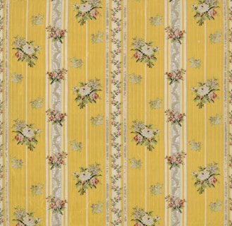 A floral patterned wallpaper featuring vertical yellow stripes with intricate floral bouquets and decorative elements in between. The flowers are arranged in small clusters with colors including white, pink, and green, adding a vintage charm to the design.
