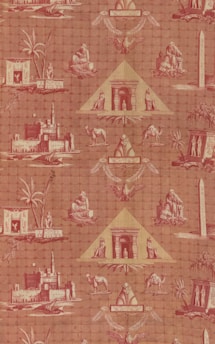 A patterned wallpaper featuring Egyptian motifs, including pyramids, sphinxes, camels, and palm trees. The design incorporates various Egyptian symbols and structures such as obelisks, making use of a reddish color palette.