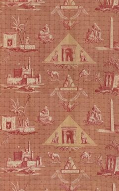 A patterned wallpaper featuring Egyptian motifs, including pyramids, sphinxes, camels, and palm trees. The design incorporates various Egyptian symbols and structures such as obelisks, making use of a reddish color palette.