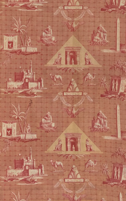 A patterned wallpaper featuring Egyptian motifs, including pyramids, sphinxes, camels, and palm trees. The design incorporates various Egyptian symbols and structures such as obelisks, making use of a reddish color palette.