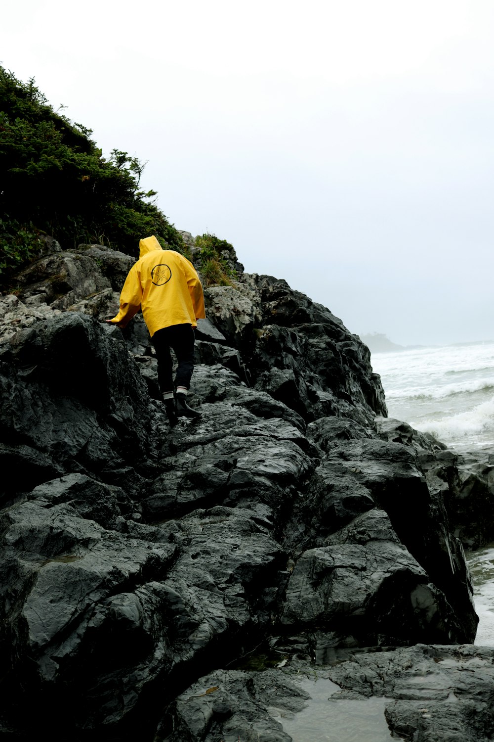 a person in a yellow jacket walking on rocks near the ocean