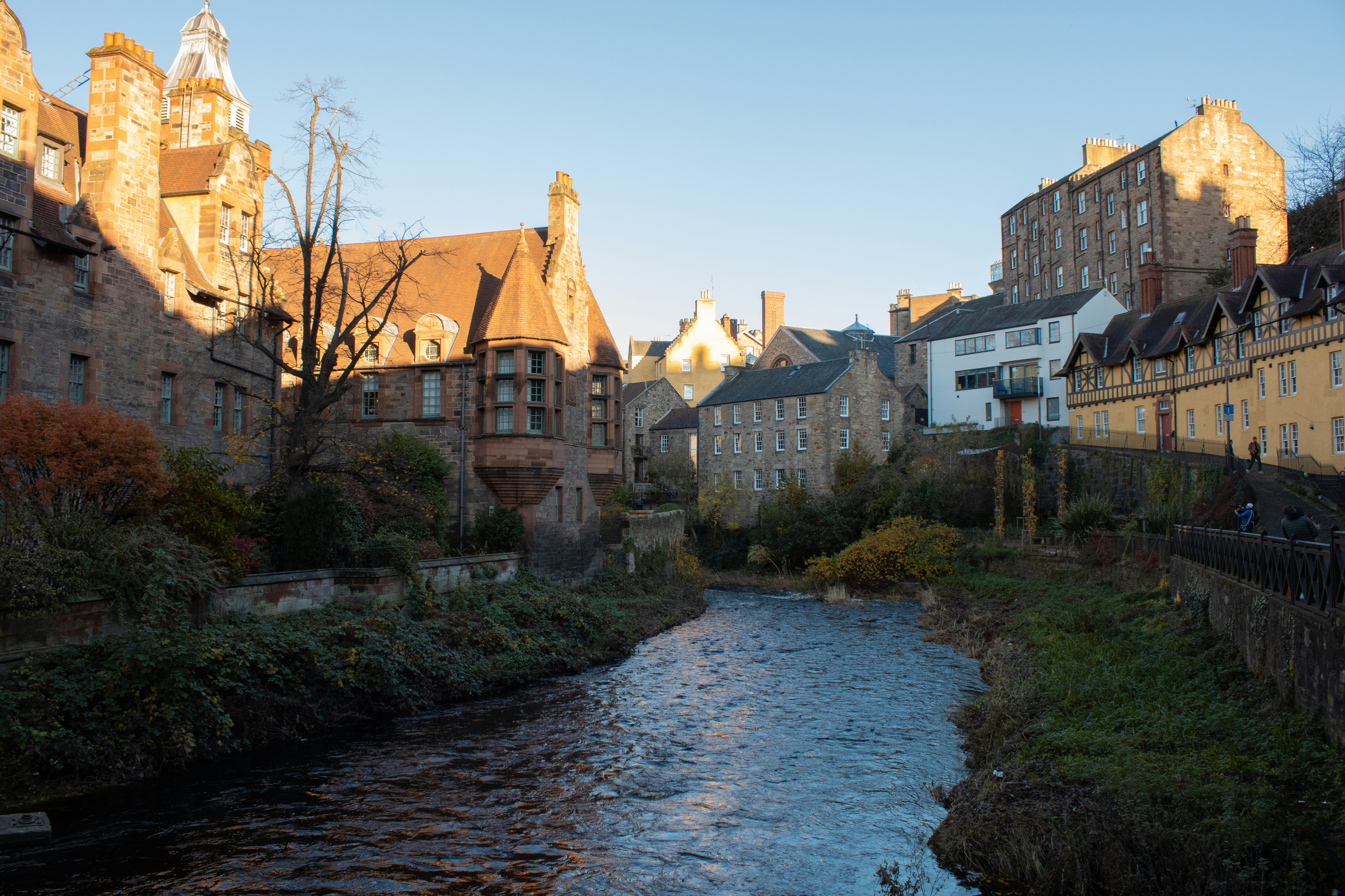 a river running through a city next to tall buildings, dean village in the afternoon sun