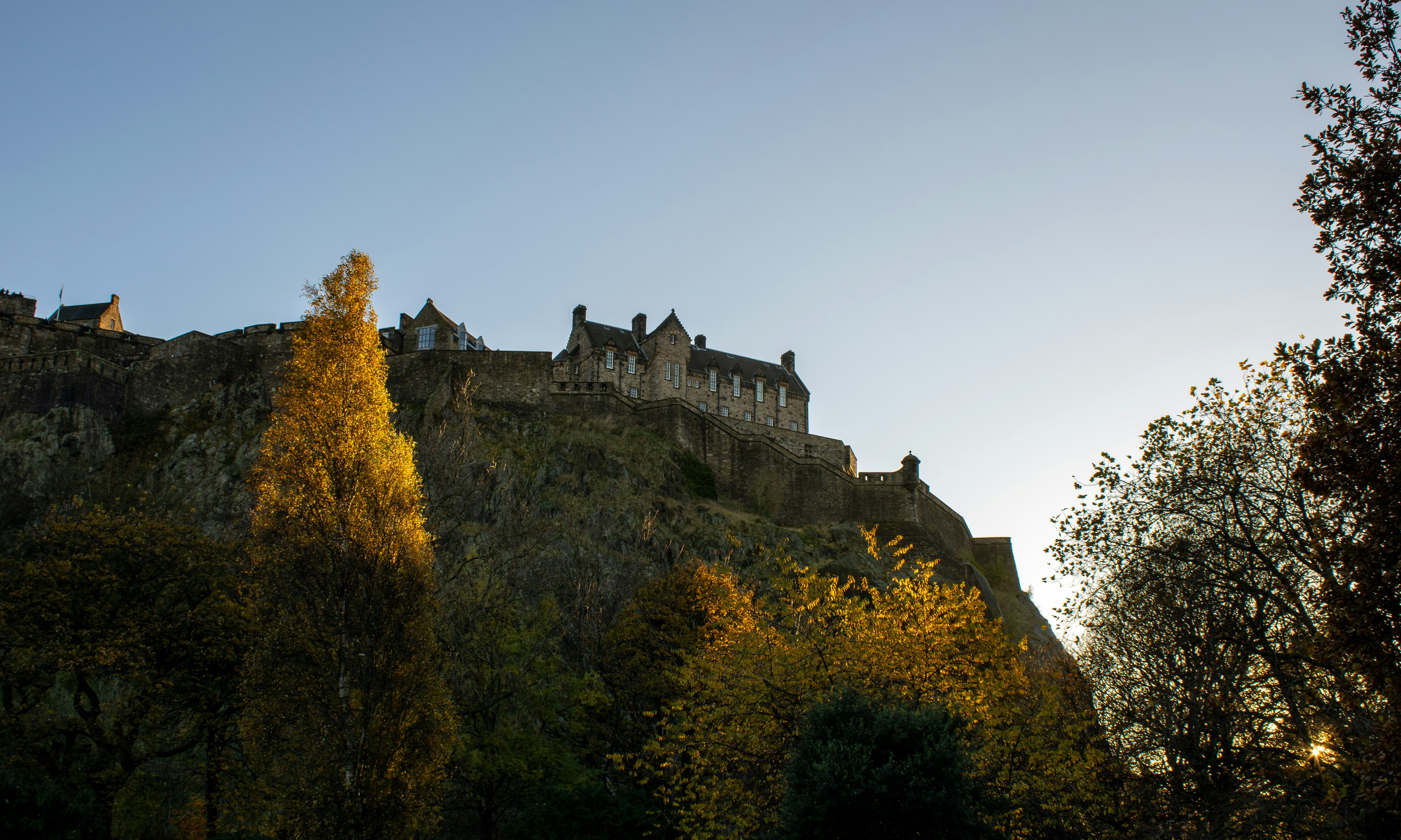 a castle on top of a hill surrounded by trees, a view of Edinburgh Castle from Princes Street gardens